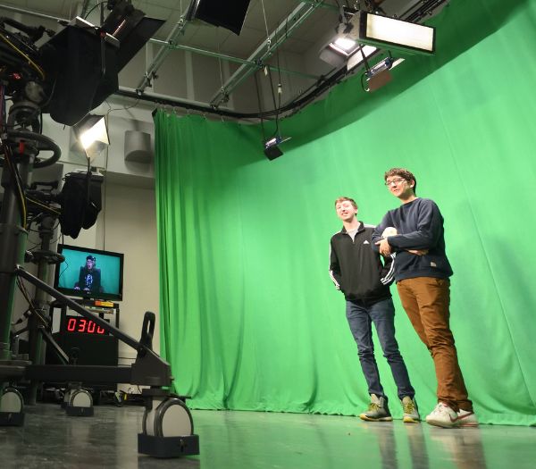 University of Akron students stand in front of a green screen while filming in a campus television studio.